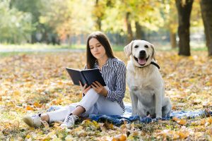 Mulher lendo livro ao ar livre com cachorro