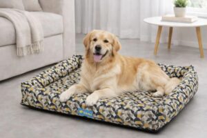 Cão Golden Retriever deitado e sorridente em uma cama retangular com estampa geométrica amarela, cinza e preta, com bordas elevadas acolchoadas, em uma sala de estar.